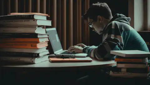 Una persona che studia con un computer portatile e dei libri davanti a sé, rappresenta la preparazione necessaria per superare l'esame di certificazione CompTIA Security+.