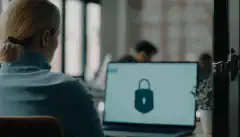 Un'immagine di una persona seduta alla propria postazione di lavoro con un lucchetto di sicurezza in primo piano, a indicare l'importanza di proteggere le postazioni di lavoro.